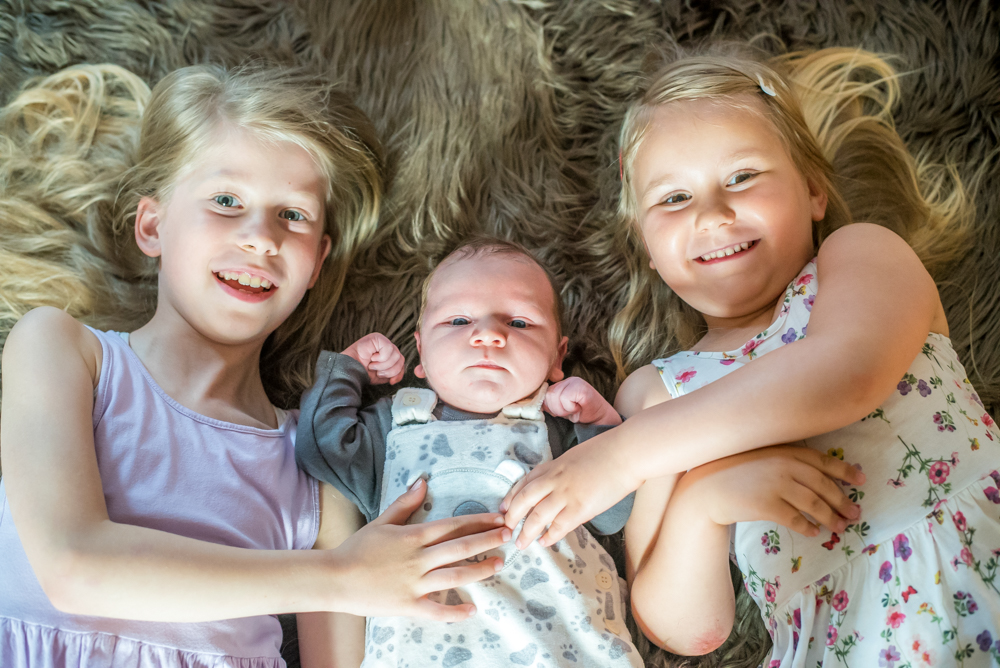 Sisters cuddling baby brother, newborn photographer Cockermouth